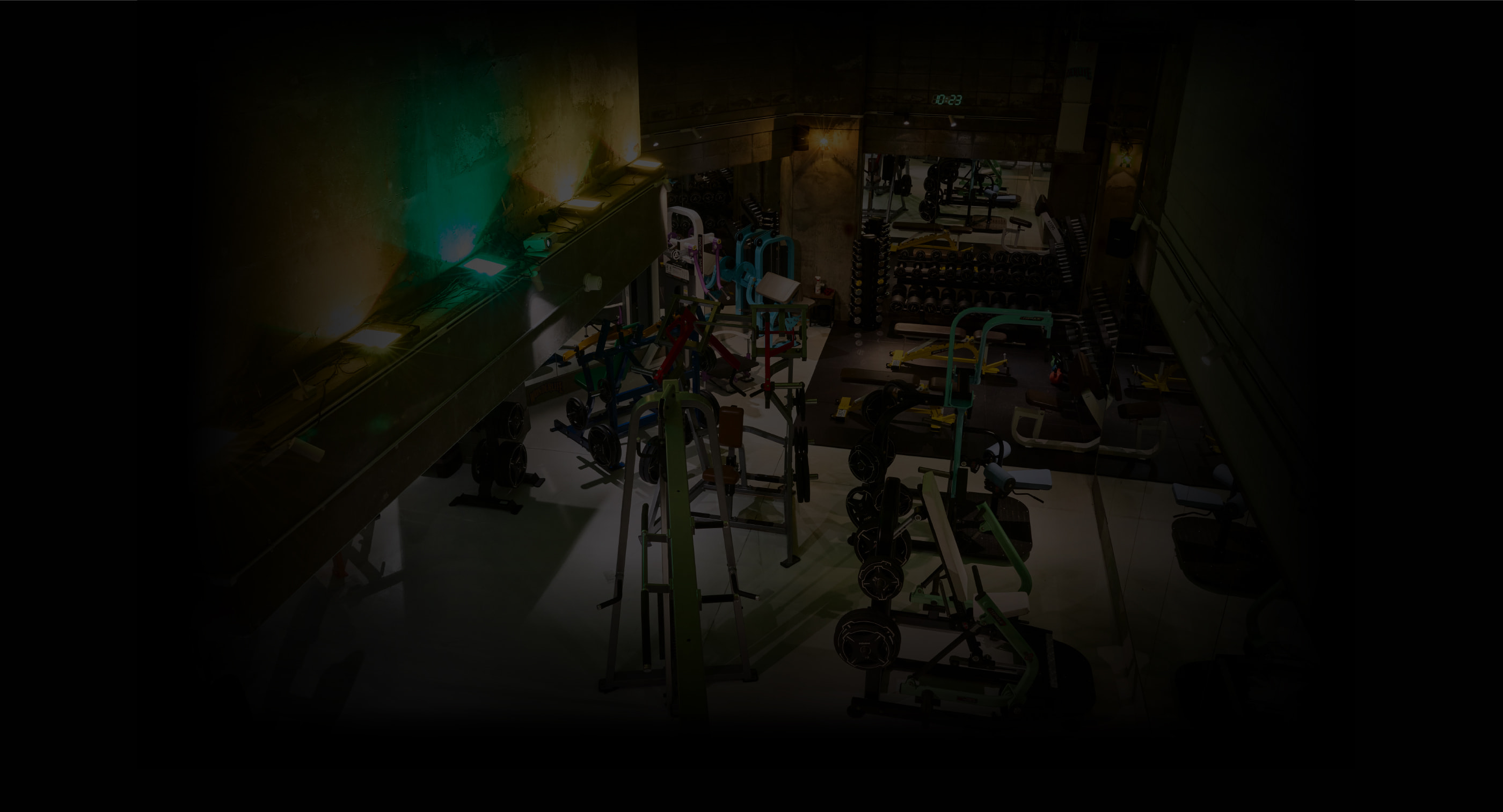 暗い照明の中でトレーニング器具が並ぶジムの内観