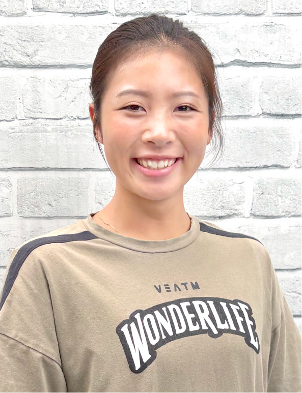 白い背景の前で笑顔を見せる女性トレーナーのポートレート写真